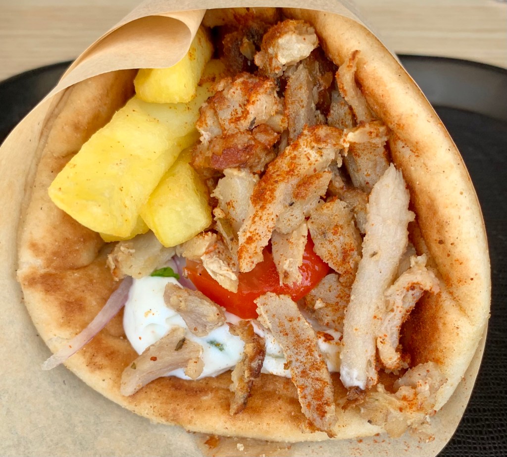 Apetyczny gyros w picie z frytkami, mięsem, sosem tzatziki i pomidorem, zawinięty w papier i posypany papryką.