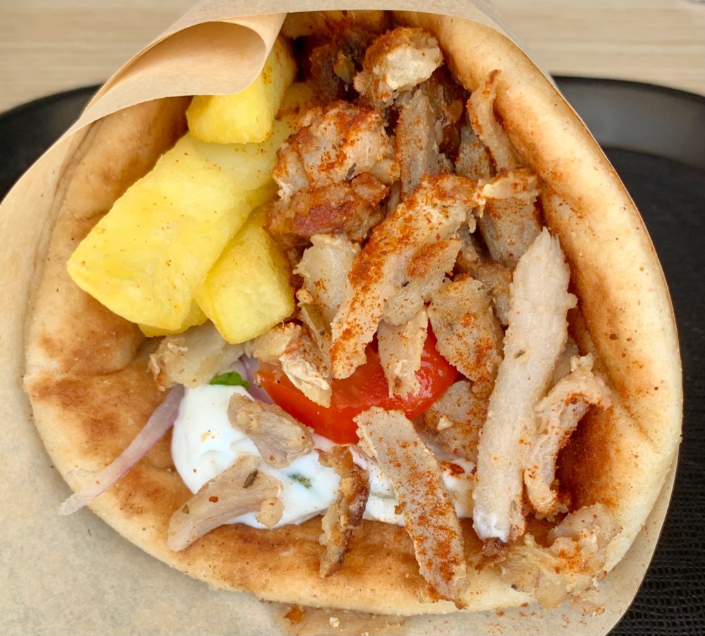 Apetyczny gyros w picie z frytkami, mięsem, sosem tzatziki i pomidorem, zawinięty w papier i posypany papryką.