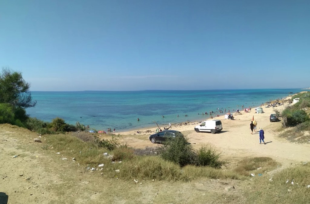 Plaża Hammametu widziana z wydmy, gdzie błękitna woda kontrastuje z jasnym, piaszczystym brzegiem.