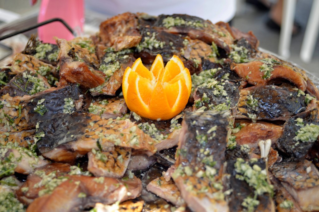 Stos grillowanych ryb udekorowany ozdobnie wyciętą pomarańczą, podkreślający świeżość i smak potrawy.