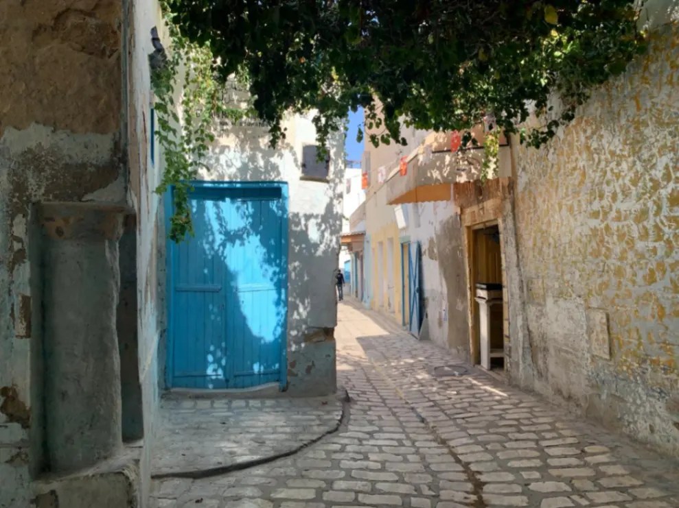 Klimatyczna, pusta uliczka medyny w Hammamecie z charakterystycznymi błękitnymi drzwiami i bielonymi ścianami.