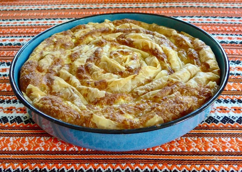 Bałkańska pita warzywna podana w okrągłym naczyniu, z chrupiącym ciastem.