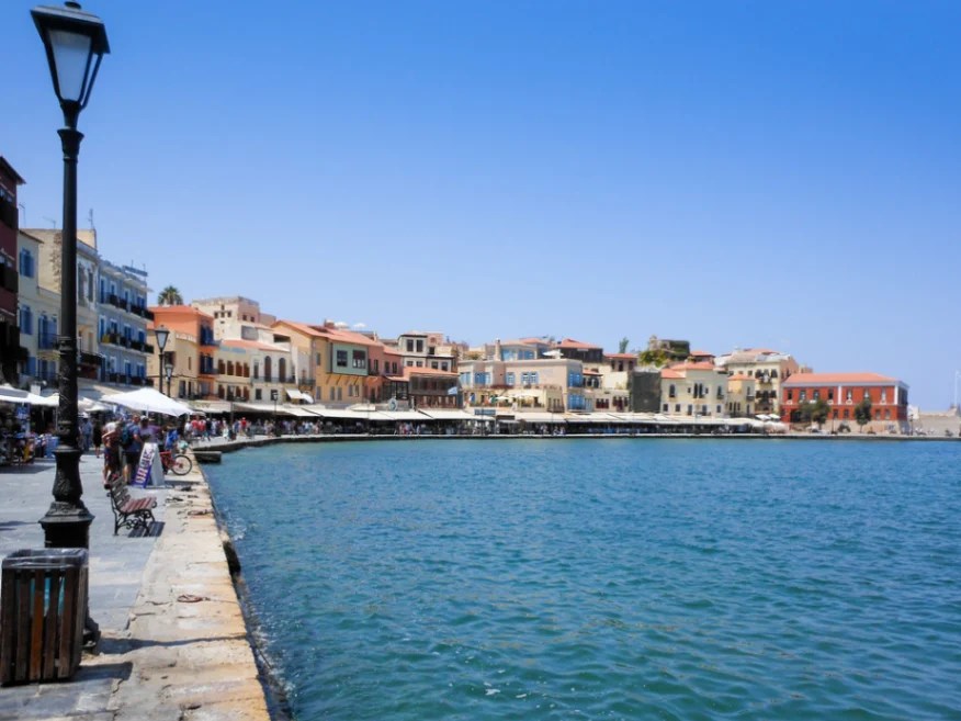 Stary wenecki port w Chanii z kamiennym bulwarem i rzędem kolorowych budynków nad brzegiem morza.