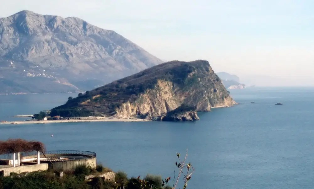 Wyspa Sveti Nikola widziana z brzegu, z tłem gór i spokojnego morza.